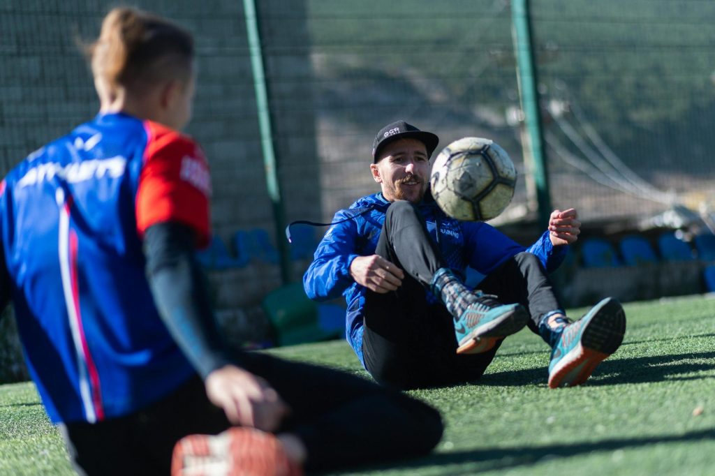 Deux joueurs de football en tenue de sport s'entraînant au contrôle du ballon à l'extérieur par une journée ensoleillée.