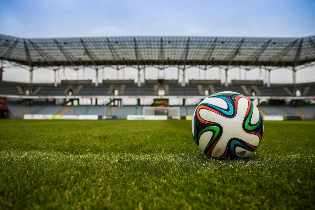 Gros plan d'un ballon de football sur un terrain d'herbe luxuriante avec un stade vide en arrière-plan.