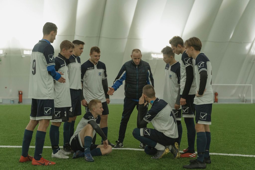 Un entraîneur de football donne des conseils tactiques à une équipe de jeunes en salle sur du gazon artificiel.