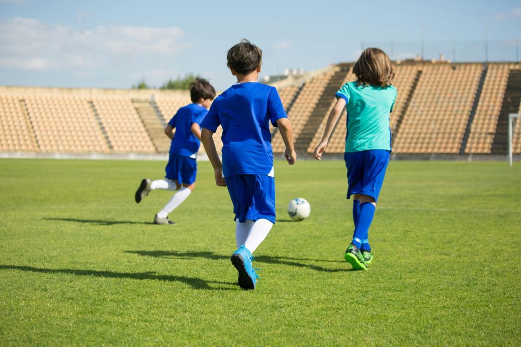 Trois enfants jouent au football sur un terrain extérieur lumineux, profitant du travail d'équipe et du sport.