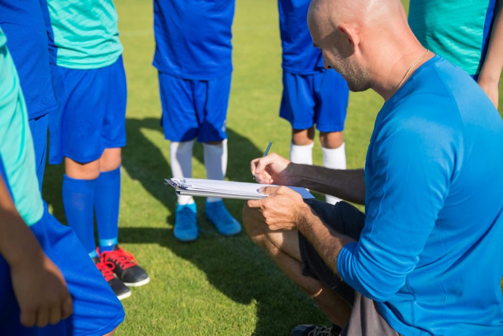 Un entraîneur de football planifie une stratégie avec de jeunes joueurs sur un terrain ensoleillé